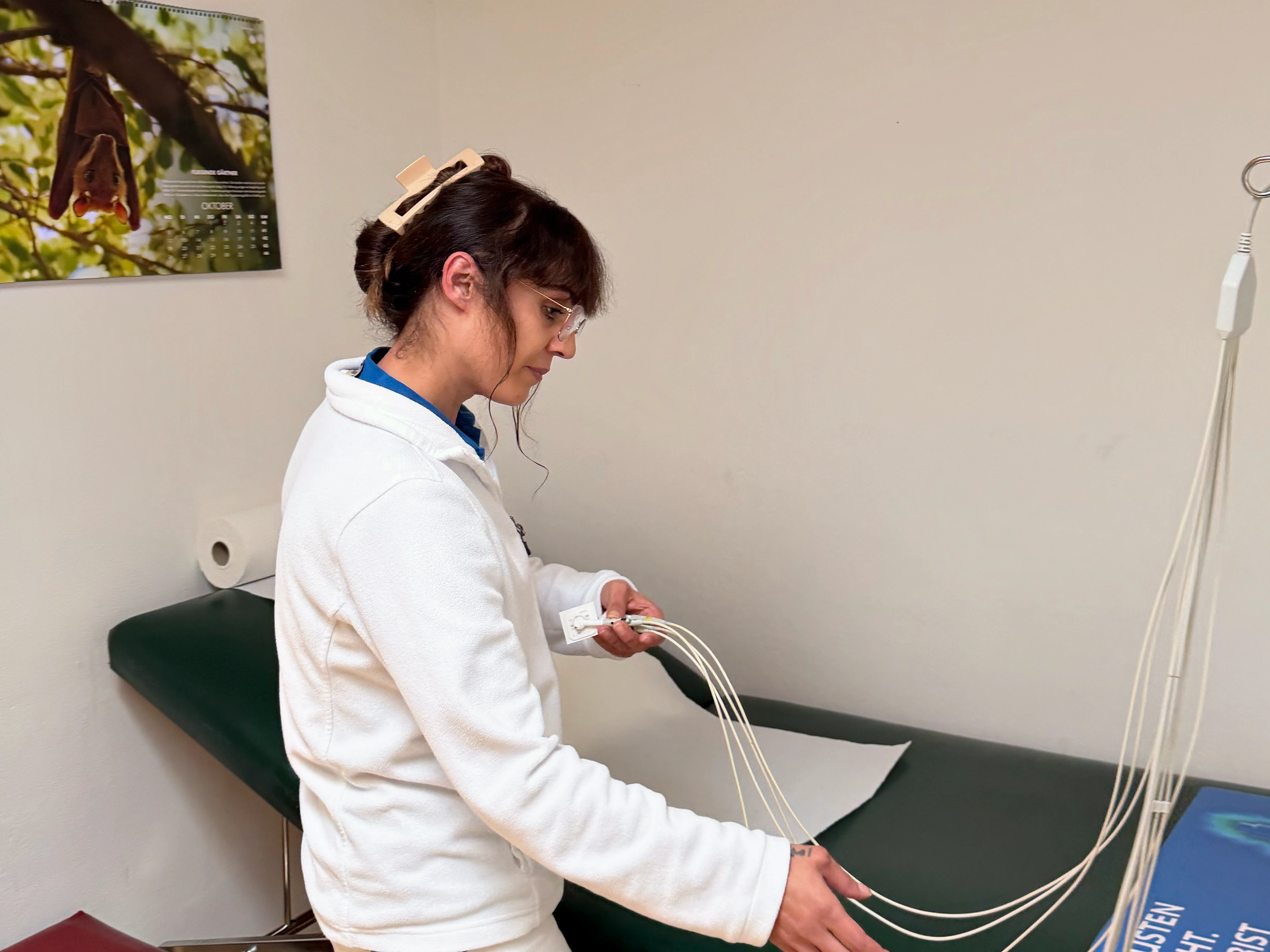 Eine Mitarbeiterin bereitet die EKG-Kabel neben der Untersuchungsliege vor.